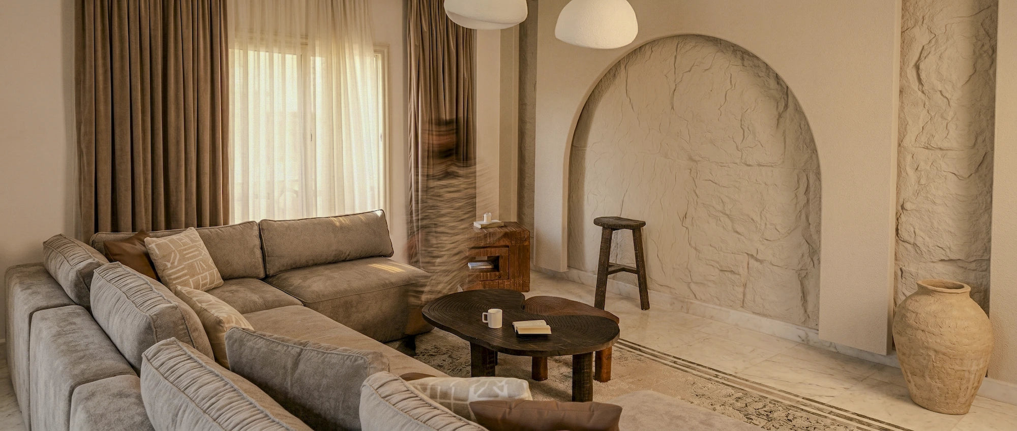 Luxurious minimalist living room with warm sunlight streaming through large windows, featuring a sustainable oak sofa and artisan woven textiles